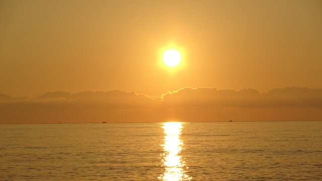 Sunrise Rising Above Cloud Layer Over Peaceful Sea.
A scenic sunrise with the sun glowing bright above a low cloud layer over the wide calm ocean surface.