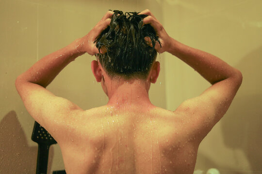 Rear View of Young Man Washing hair Under Running Water in Shower with Wet Back and Droplets on Skin