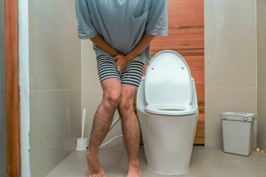 Man Holding His Groin While Crossing Legs Near Toilet Bowl, Holding Back Urge to Urinate in Bathroom