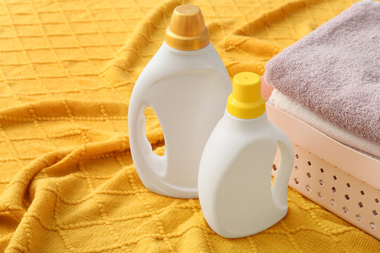 Laundry day essentials, detergent and fabric softener bottles with clean towels in a basket on a yellow blanket