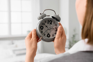 Woman setting time on alarm clock in bedroom, closeup. Daylight saving time concept