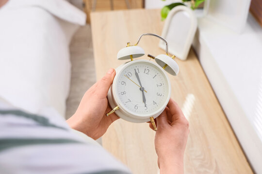 Woman changing clock for daylight saving time in bedroom, closeup