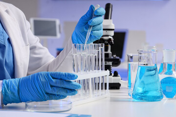 Fototapeta premium Female scientist dropping water sample into test tube at table in laboratory, closeup