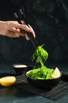 Young woman eating tasty seaweed salad with lemon on blue grunge background