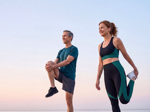 Happy middle-aged couple stretching outdoors, enjoying an active lifestyle and morning exercise together on the beach.