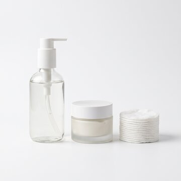 Skincare products including a pump bottle of liquid, a jar of cream, and a stack of cotton pads