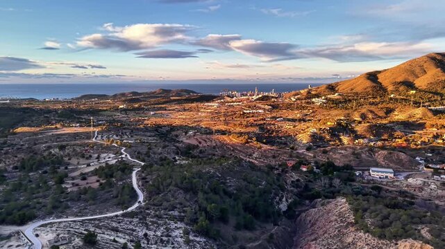 Dusk aerial trail leading to coast, drone scout capturing winding path through hills, distant city skyline,