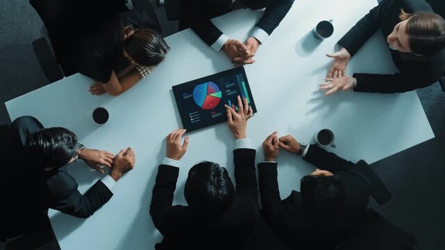 Top down aerial view of professional businessman analyze stock market chart with tablet with investment graph placed at table while investor group pointing at tablet. Creative business. Directorate.