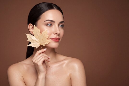 Beautiful woman with smooth skin holding a dry maple leaf near her face