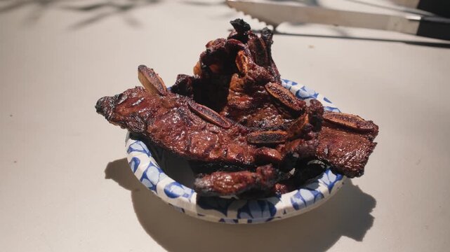 Tender cooked beef ribs with a dark smoky crust are stacked on a paper plate and ready to serve at a barbecue