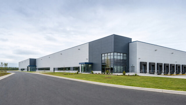 Modern industrial building exterior, grey and white facade architecture, paved road and green lawn, commercial warehouse structure, business facility, logistics center, blue sky