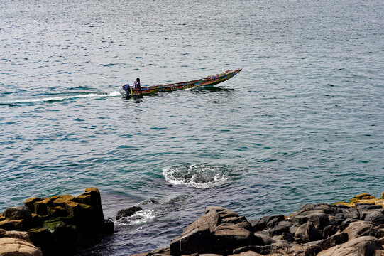 A traditional wooden pirogue boat navigates coastal Atlantic waters near a rocky volcanic shoreline on Gor&eacute;e Island, Senegal