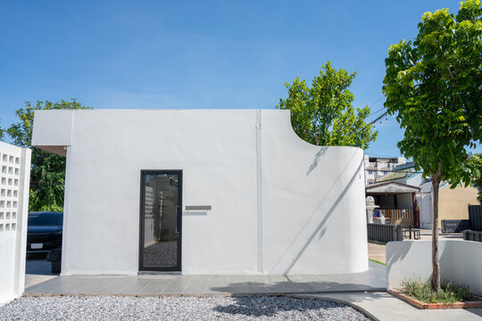 modern minimalist white concrete cafe building exterior with a sleek glass door and curved wall architecture under a bright blue sky, creating an inviting hospitality destination.