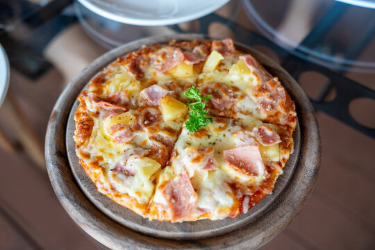 Freshly baked Hawaiian pizza slices topped with savory ham, sweet pineapple, and melted cheese, served on a round wooden board in a warm restaurant setting for a delicious meal.
