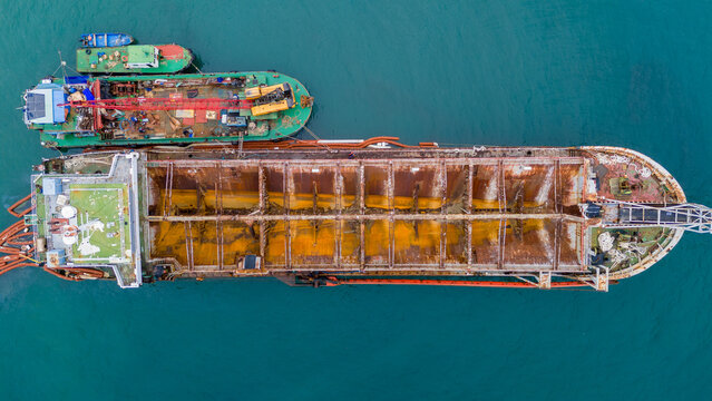 Old heavily rusted industrial cargo ship floating in the blue ocean. Detailed view of decaying metal hull and maritime transport infrastructure reflecting heavy wear and tear.