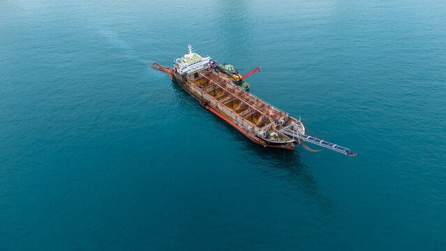Old heavily rusted industrial cargo ship floating in the blue ocean. Detailed view of decaying metal hull and maritime transport infrastructure reflecting heavy wear and tear