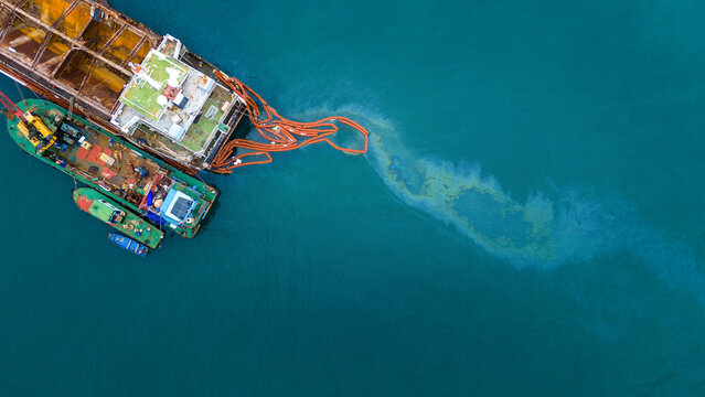 Oil spill Industrial response ship deploying an orange containment boom to control and clean up a marine pollution spill in the open ocean, protecting the sea ecosystem from hazardous chemical waste.