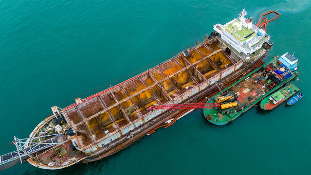 Old heavily rusted industrial cargo ship floating in the blue ocean. Detailed view of decaying metal hull and maritime transport infrastructure reflecting heavy wear and tear.