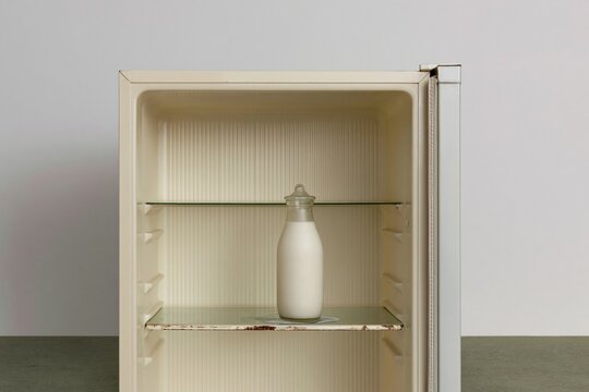 Open empty refrigerator with a single glass bottle of milk on a shelf, featuring muted pastel tones and copy space for minimal living and food storage