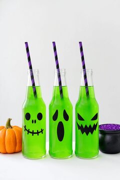 Three glass bottles with green Halloween drinks and spooky ghost faces on white background