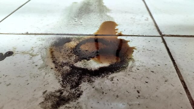 Engine oil leak stains on a dirty white tiled floor, set against a workshop or garage background