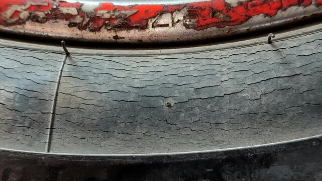 The cracked motorcycle tire shows severe rubber deterioration due to aging and wear, necessitating immediate replacement for safety reasons