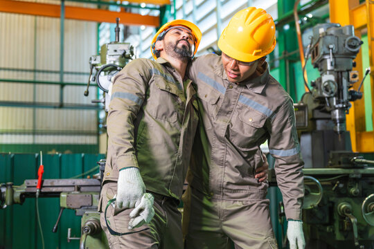 Injured factory worker being helped by colleague after workplace accident in plant, coworker supporting injured industrial technician suffering from pain in workshop, accident and first aid assistance