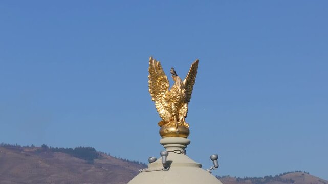 Golden eagle statue sits atop a capitol dome against a clear blue sky