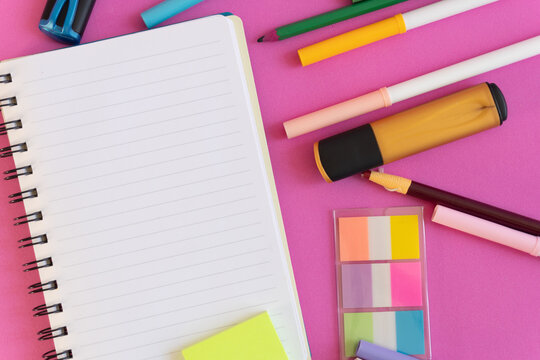 Bright stationery items arranged neatly beside open spiral notebook