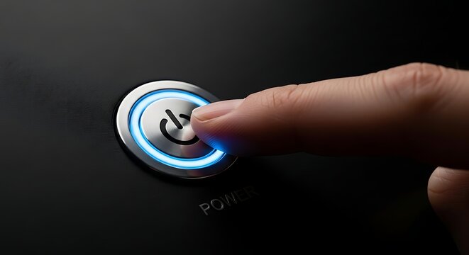 Finger pressing illuminated power button on black surface with the word power below