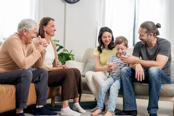 Obraz na płótnie Canvas Caucasian father guides young son's hands while mother and grandparents watch with smiles on sofa, presenting nurturing parenting, family attention, supportive learning, and quality time together.
