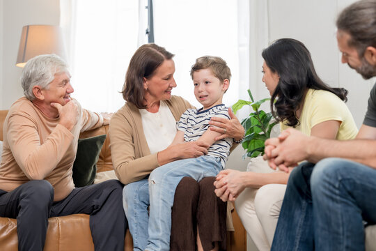 Caucasian grandmother supports grandson on lap while mother talks and grandfather listens, presenting nurturing care, family communication, emotional support, and multigenerational togetherness.