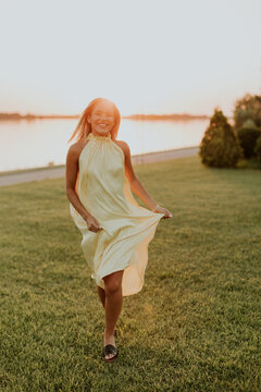 Woman walks on grass near river at sunset wearing a light dress