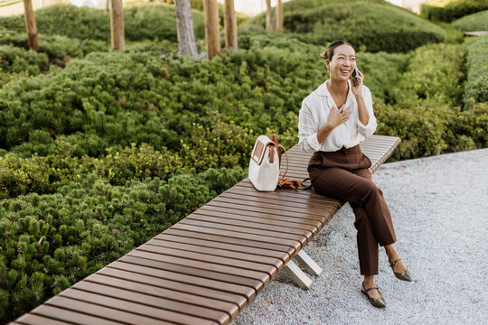 Laughing woman enjoying a phone conversation in a lush park setting