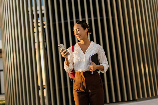 Korean woman smiles while checking her smartphone in a modern urban setting