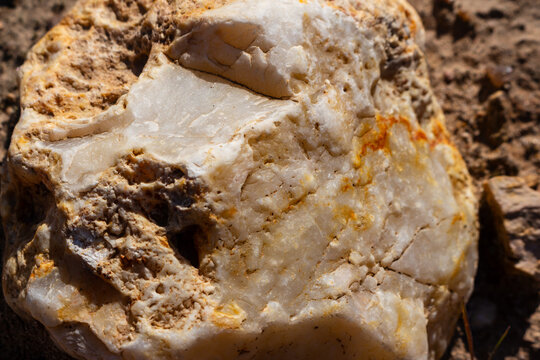 Close-up of a raw chalcedony flint stone with a rugged, weathered surface texture resting on moraine ground, showcasing natural geological mineral formations in bright sunlight