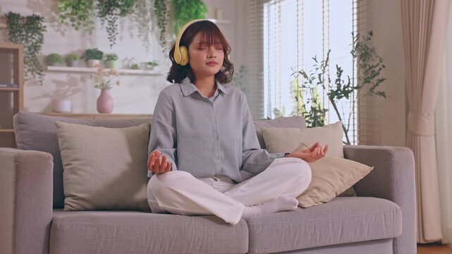 Woman Meditation Headphone Sofa Living Room Indoor Calm Relaxation Plant Home Wellness Mindfulness Peaceful Young Meditating Cozy Bright Decor Gray Sofa Mindful Lifestyle