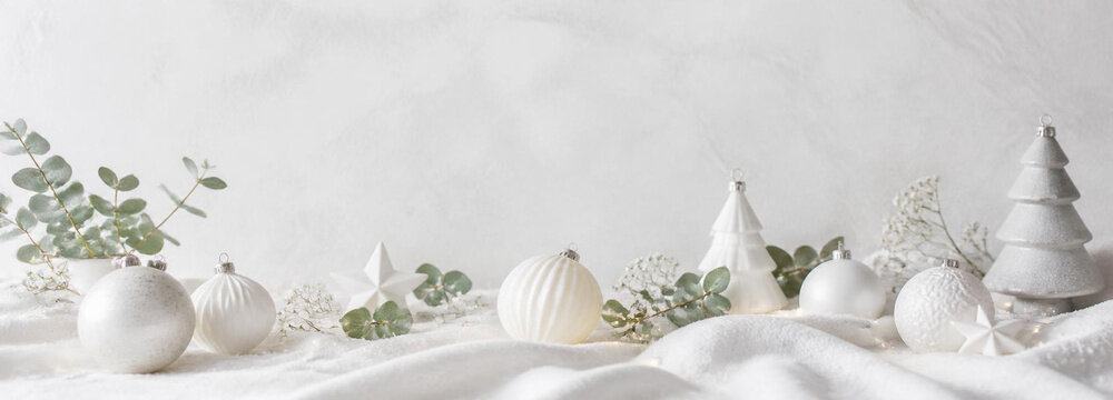 Christmas composition with white ornaments, eucalyptus branches, and decorative trees on a soft fabric background, creating a festive holiday atmosphere