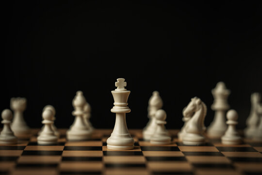 white chess king standing tall on a board, surrounded by blurred pieces on black background