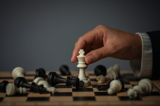 business hand holding white chess king on board with fallen pieces