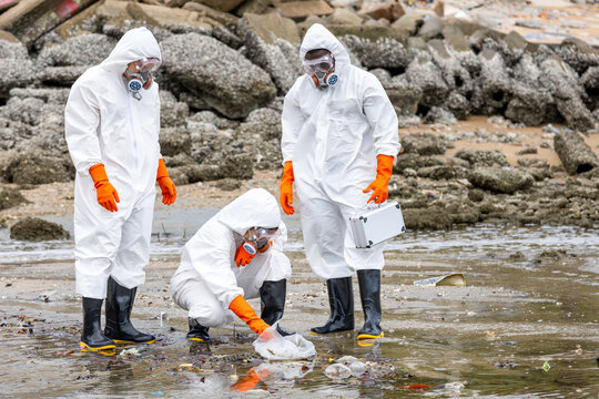 Team of scientists in hazmat suits inspecting polluted beach and collecting sample, Environmental researchers investigating toxic waste on shore, Specialists working at polluted coastal area