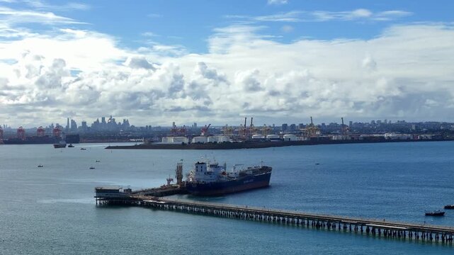 Large tanker cargo transport ship moored at long pier across Botany Bay under bright cloudy skies, aerial, Kurnell NSW Australia