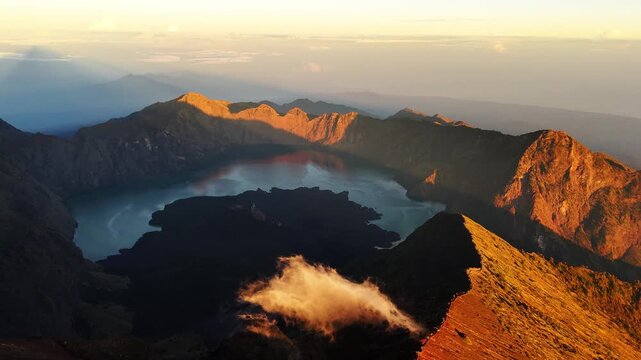 Caldera lake framed by volcanic ridges with glowing cloud at sunrise, aerial pullback with golden strong light ray beams, Rinjani Indonesia