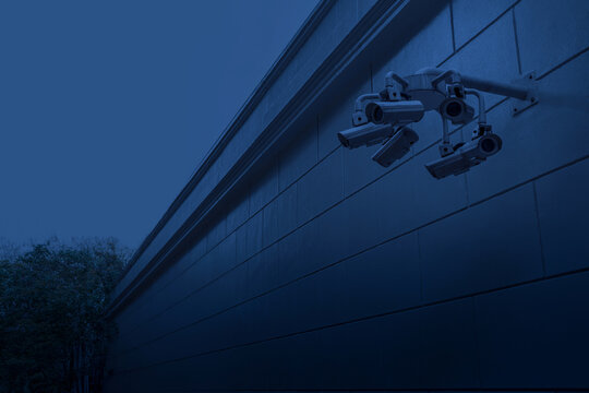 Multiple CCTV security cameras mounted on outer wall fence at night time, arranged to provide wide-area surveillance from different angles, dark and isolated soi, quiet alley, property safe, privacy