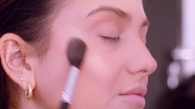 Applying highlighter. Facial procedure. Woman professional visagiste using brush cosmetic product for makeup in beauty salon.