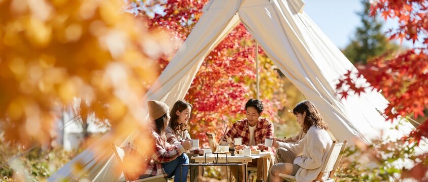 Group of friends gathering for a meal outside a tent surrounded by vibrant fall foliage
