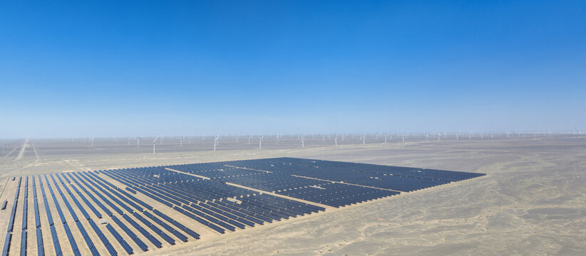 Aerial View of Vast Desert Solar Panel Farm with Wind Turbines on Horizon