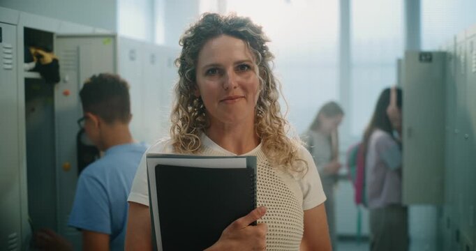 Portrait of Happy Smiling Female Teacher Holding Notebooks and Folders Standing in School Corridor with Lockers. Mentorship, Academic Support, Positive Communication in Modern School Environment.