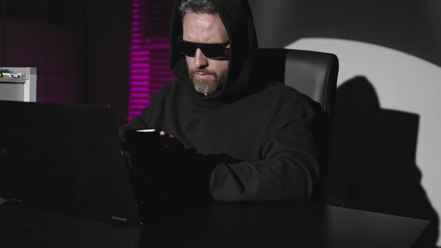 Hacker in hoodie dark night theme. Cyber hacker and data security. Office hacker typing malware at night. Hooded hacker works at office. Digital hackers attack.
