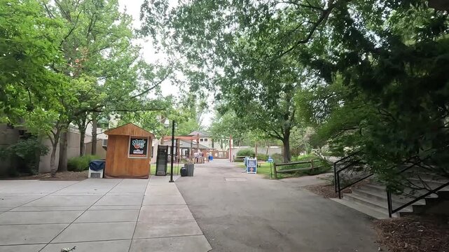 Paved pathway through Zoo Boise passing wooden kiosks and green trees.